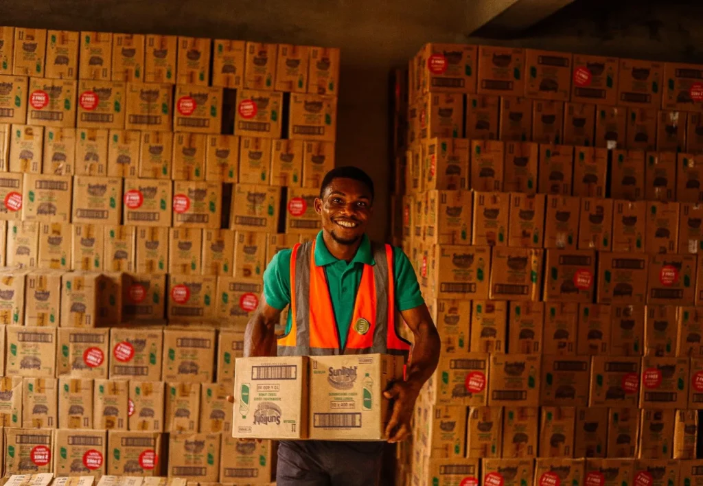 A warehouse worker carrying a carton of goods past stacked cases