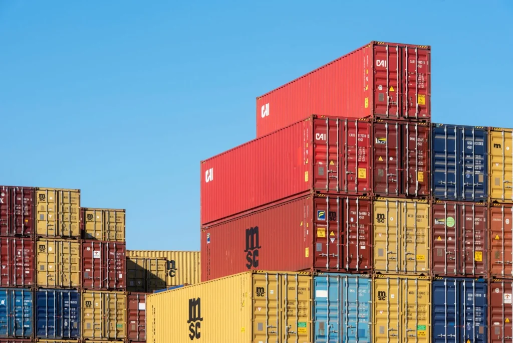 Stacks of shipping containers in a terminal yard under a clear sky